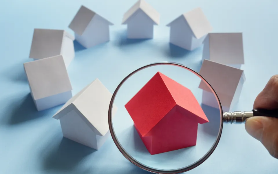 Nince toy house, eight of them are color white while the one in the middle is color red and is being magnified by a magnifying glass - LasVegasRealEstate.com