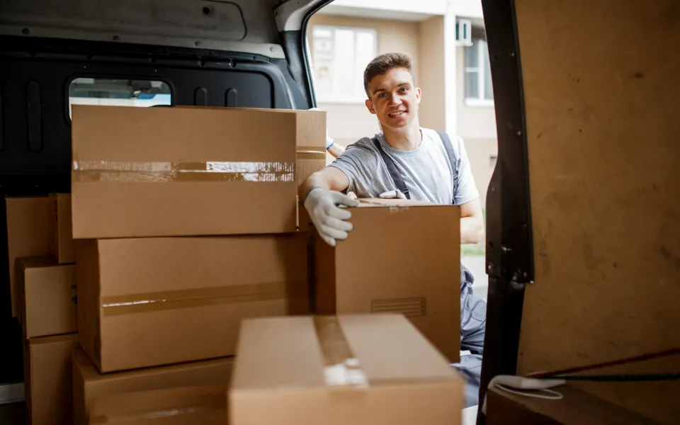 A young handsome smiling worker wearing uniform is standing next to the van full of boxes. House move, mover service - LasVegasRealEstate.com