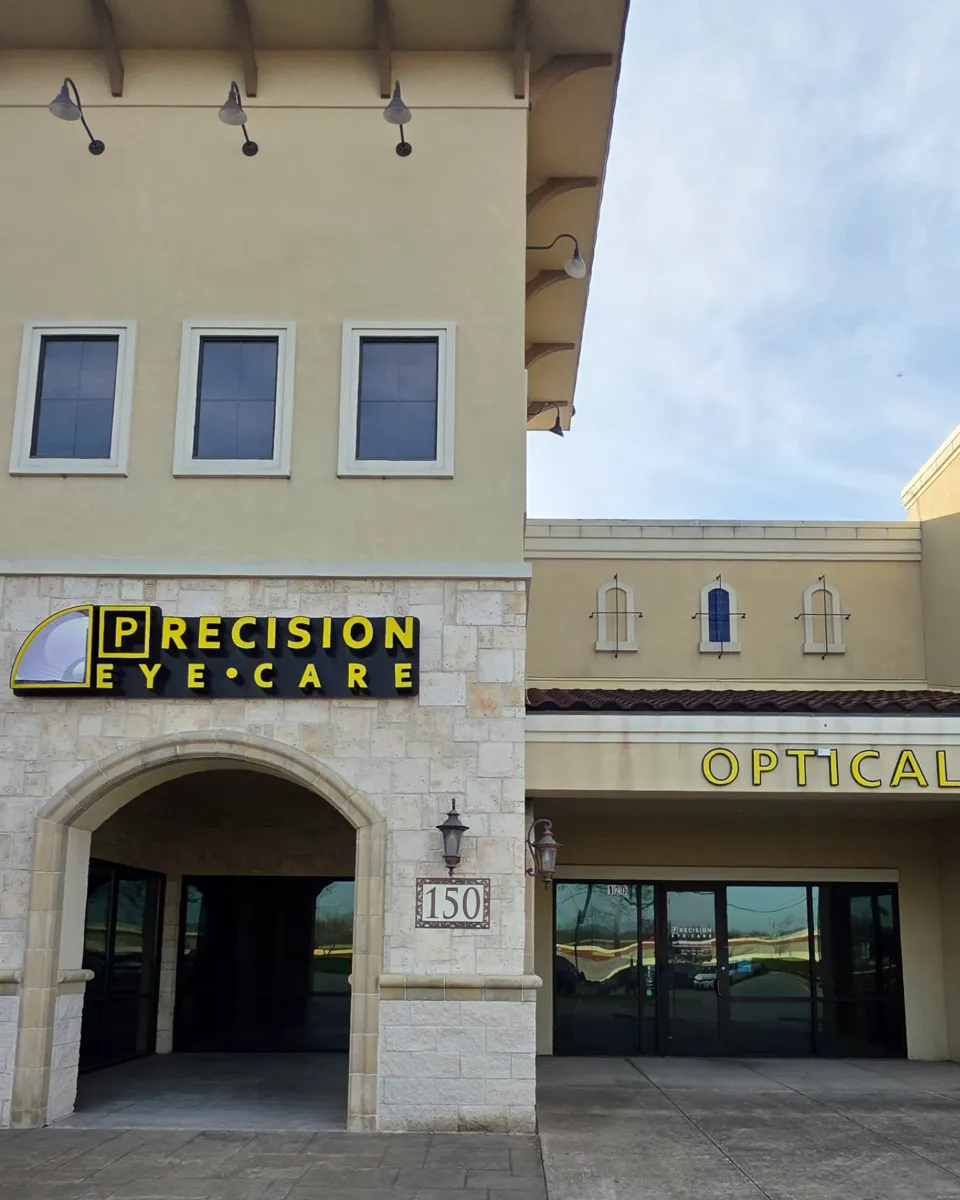 Front entrance of the Precision Eye Care Optical store building with a yellow sign and lamps