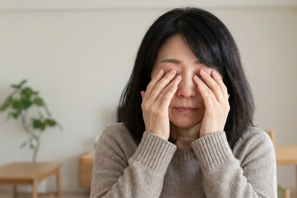 an older Asian woman sitting at a table with her hands covering her face