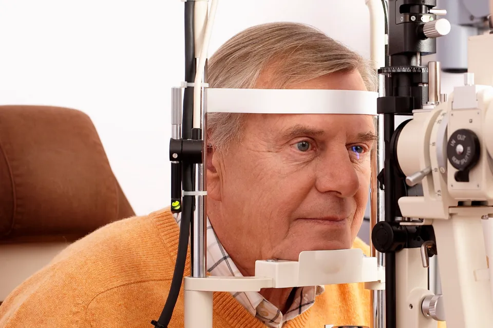 An older man is having his eyes examined by an eye doctor using a phoropter