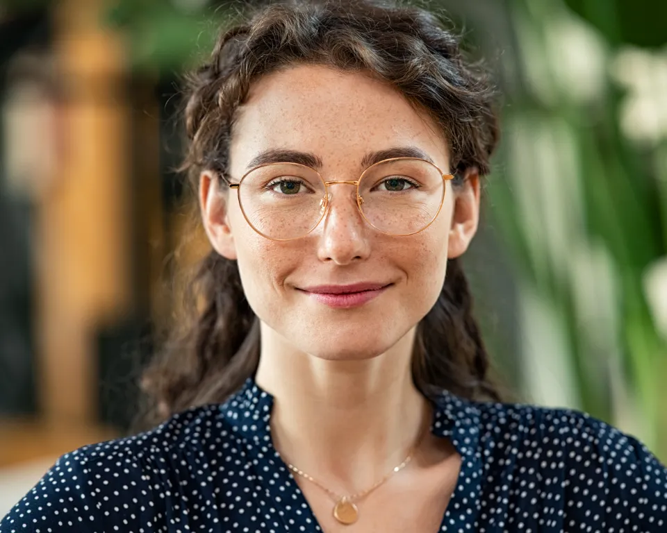 woman wearing a blue polka dot shirt and gold glasses smiling at the camera