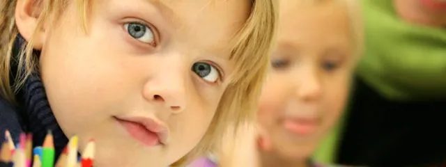 Young child with blue eyes looking up near colored pencils