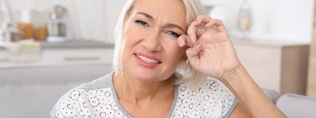 Older woman touching eye while experiencing discomfort