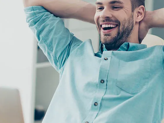 Smiling man leaning back in chair while looking at laptop
