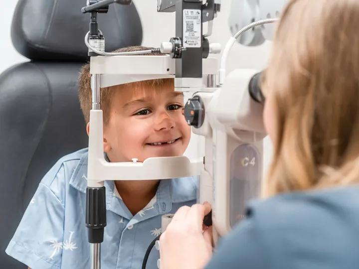 Young boy smiling during slit lamp eye exam at clinic