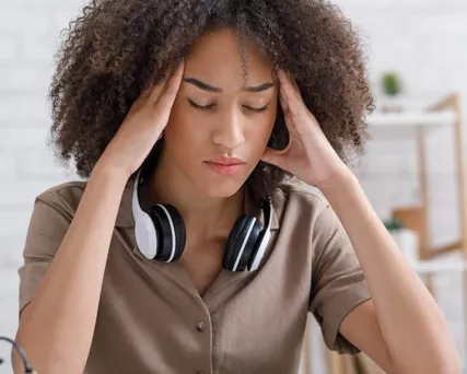 Young woman with headache holding head while studying at desk