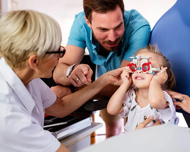Child receiving playful eye exam with parent and optometrist