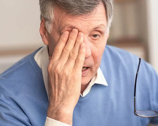 Older man rubbing one eye while holding eyeglasses in hand