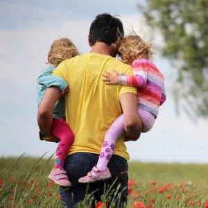 Father carrying two children through field of red wildflowers